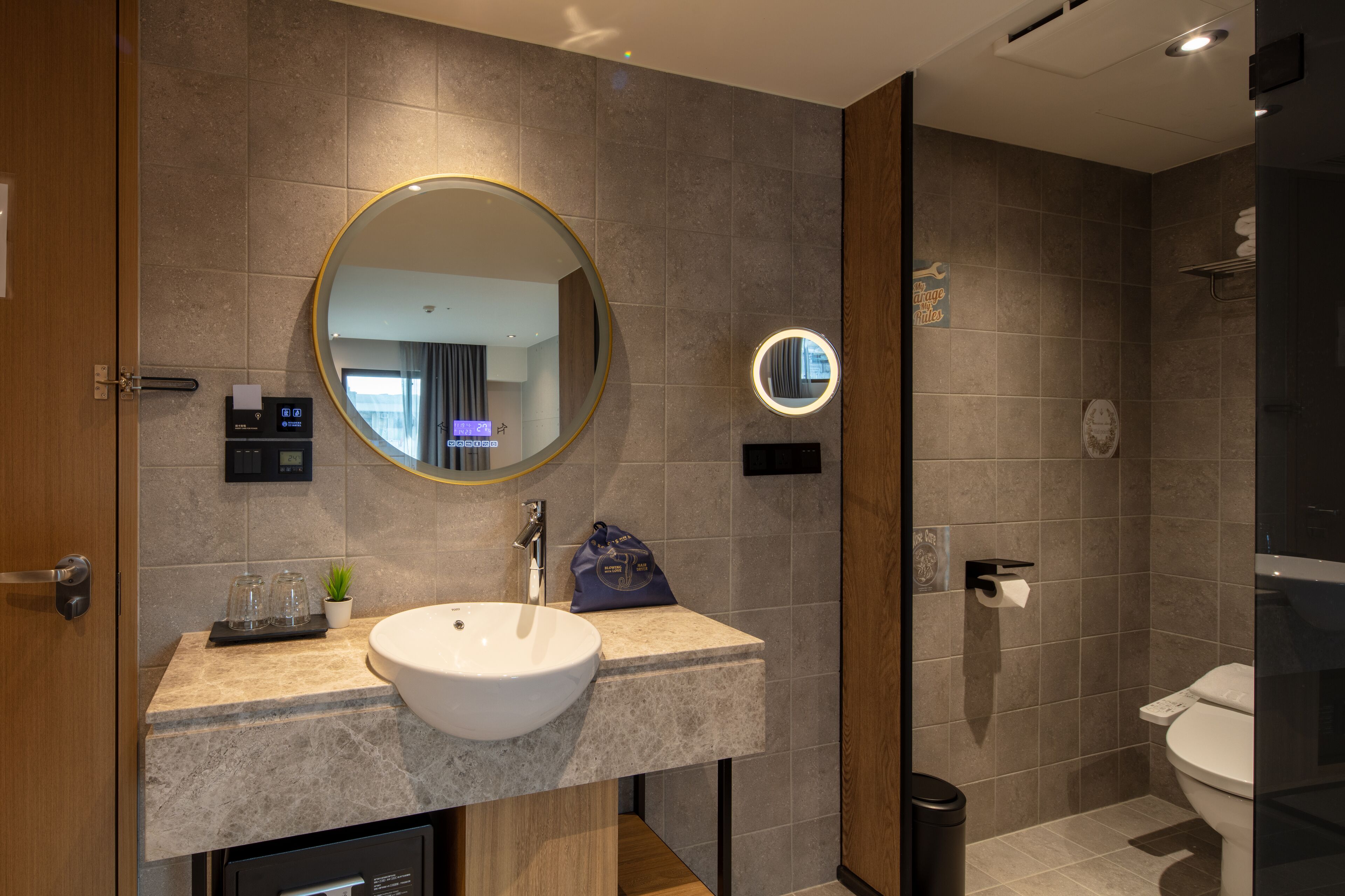 Un baño moderno con un espejo redondo grande, un lavabo, una pequeña planta en maceta y un perchero para toallas.