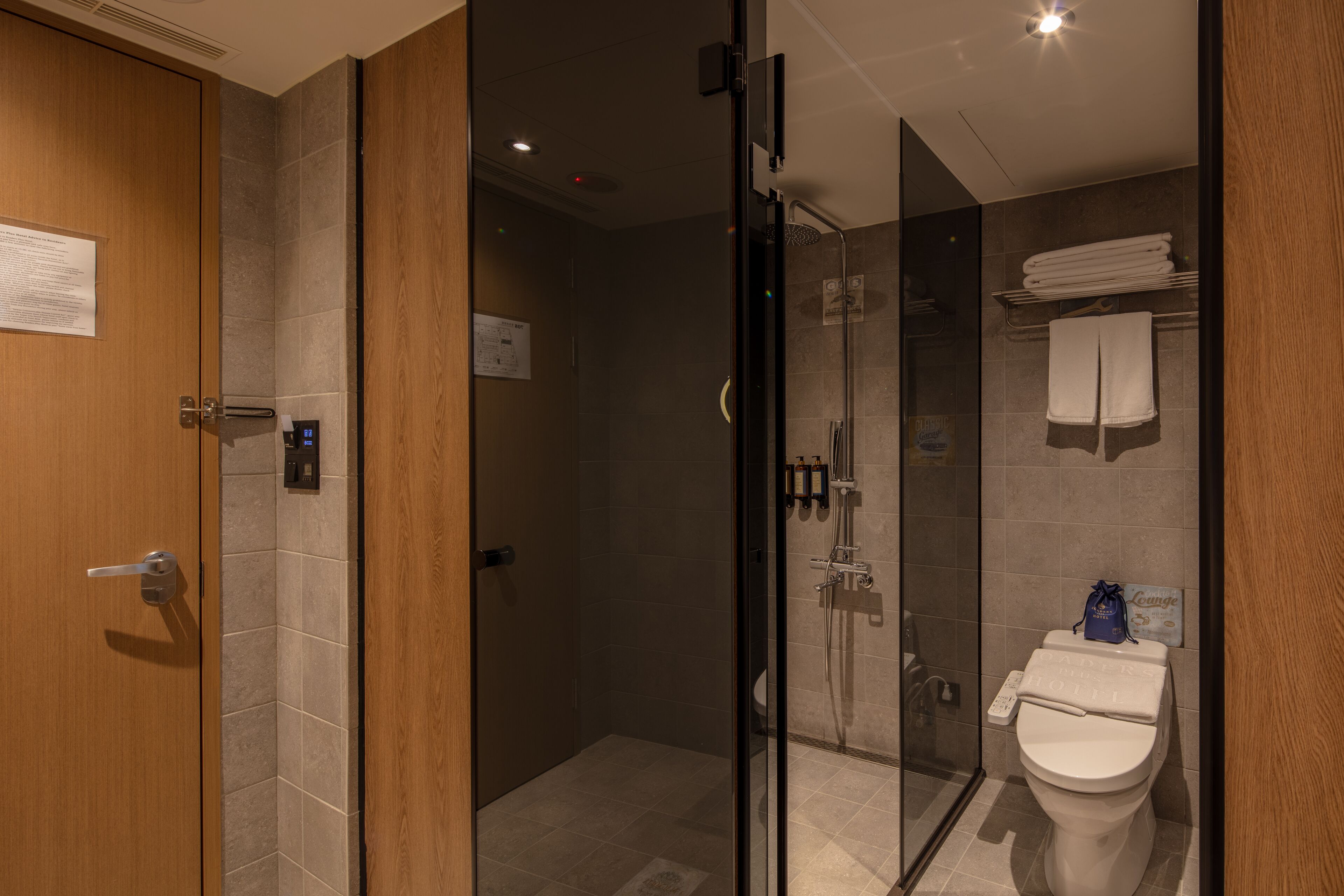 A modern bathroom with a glass shower enclosure, a toilet with a towel rack, and a wooden door.