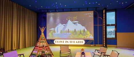 A drive-in theater with a projection screen displaying a mountain scene, a teepee, and a table with chairs and a lantern.