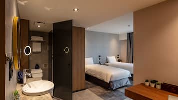 A modern hotel room with a large bathroom, two beds, a desk, and a small seating area.