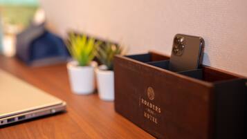 Et træskrivebord med en bærbar computer, en smartphone i en træholder og to små krukker med planter.