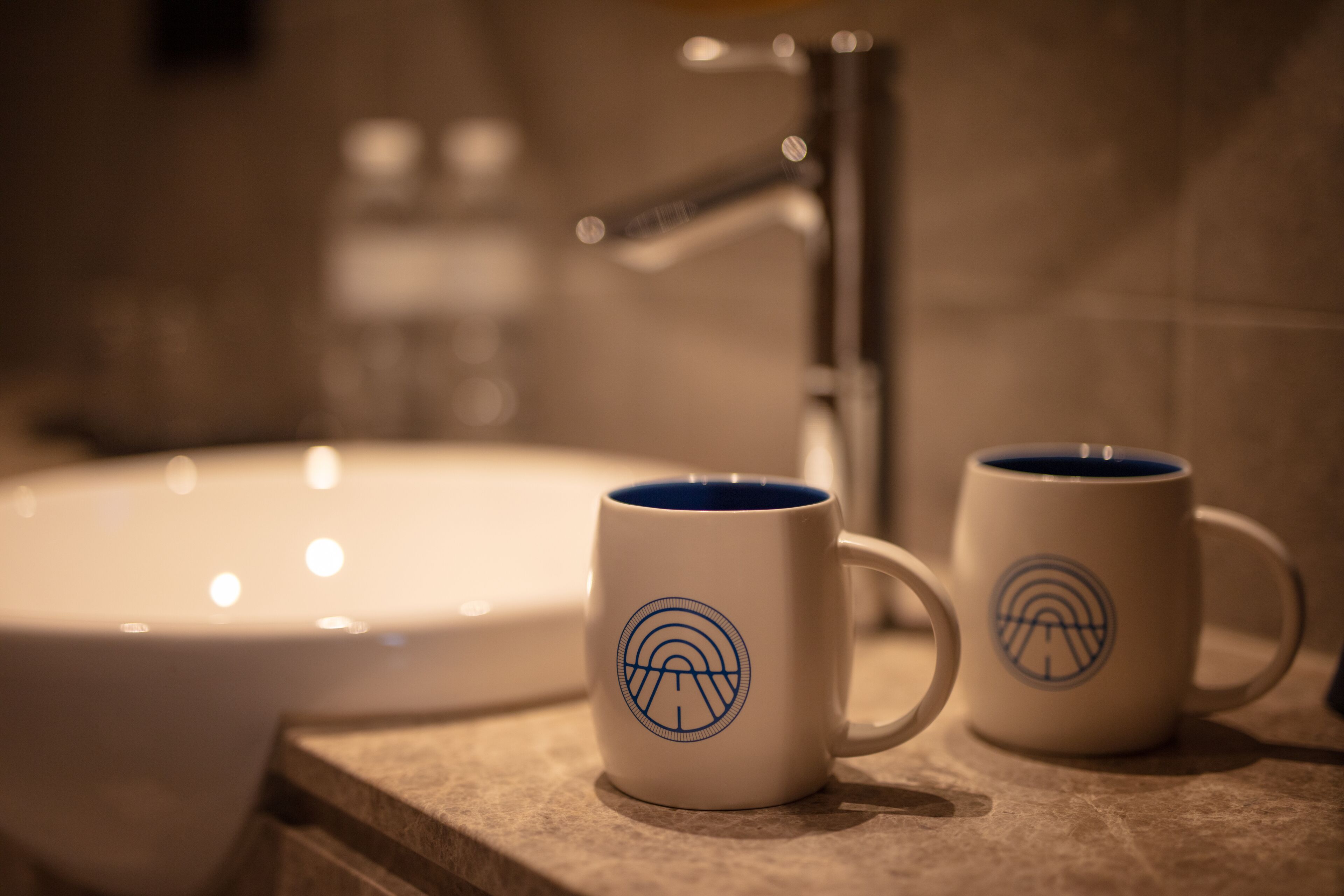 Two white mugs with blue designs on a countertop near a bathroom sink.