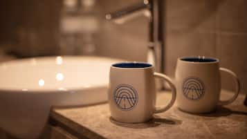Two white mugs with blue designs on a countertop near a bathroom sink.