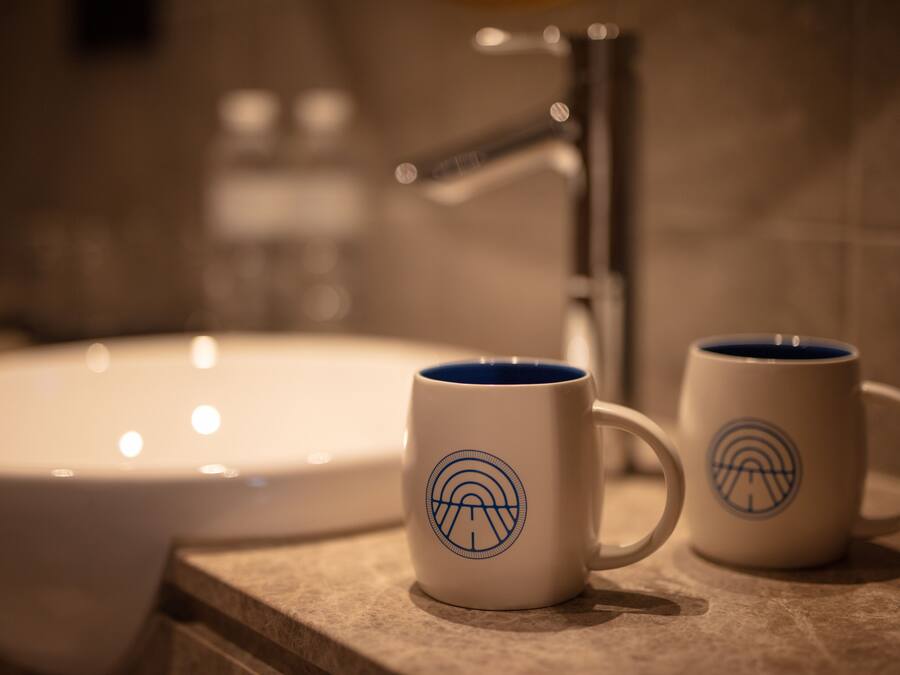 Two white mugs with blue designs on a countertop near a bathroom sink.