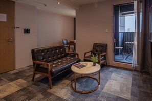 Una sala de estar moderna con un sofá de cuero, una mesita redonda y una silla. Hay una puerta con cerradura y una planta pequeña sobre la mesa.