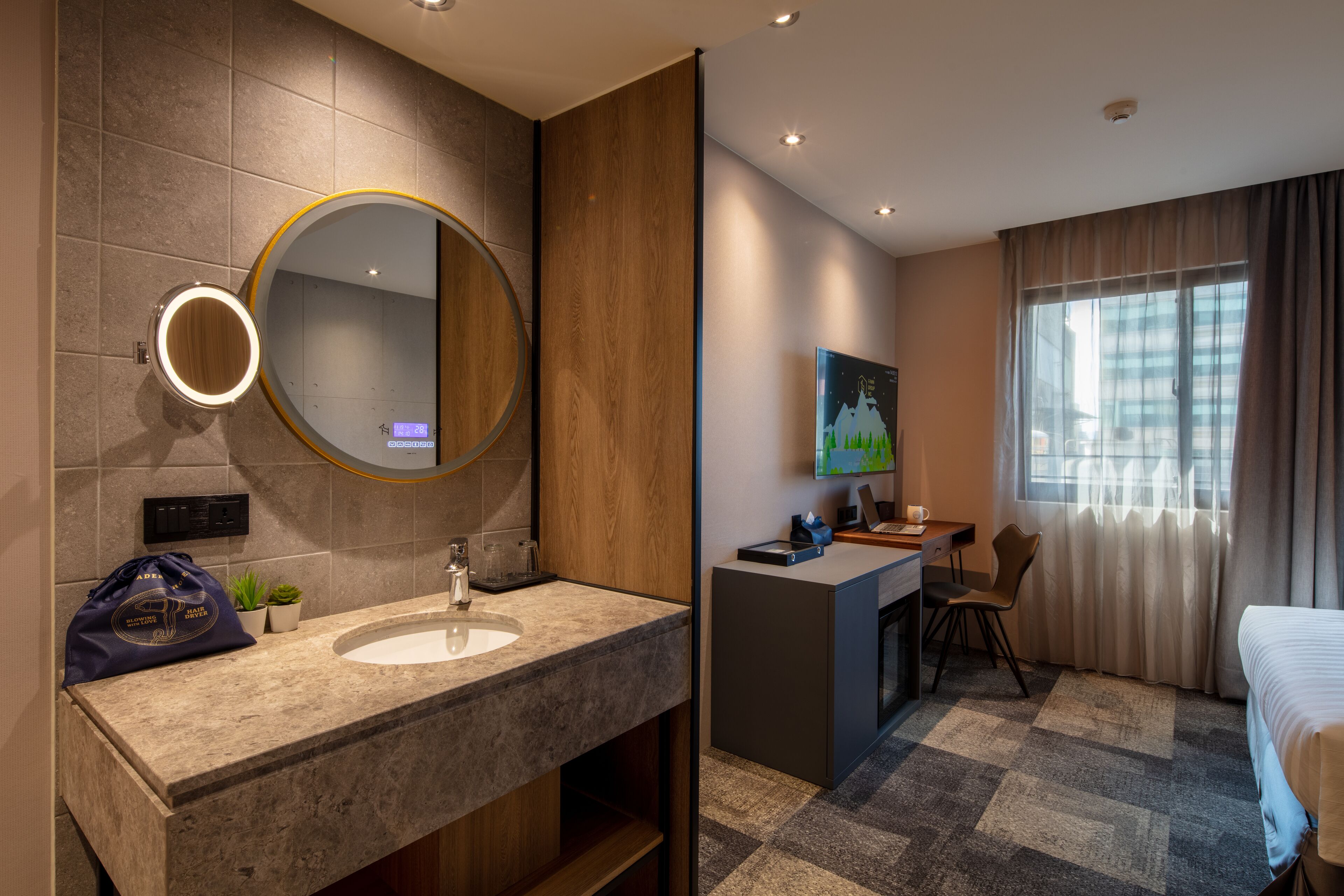 Una habitación de hotel moderna con tocador, espejo redondo, lavabo, escritorio con silla y cama.
