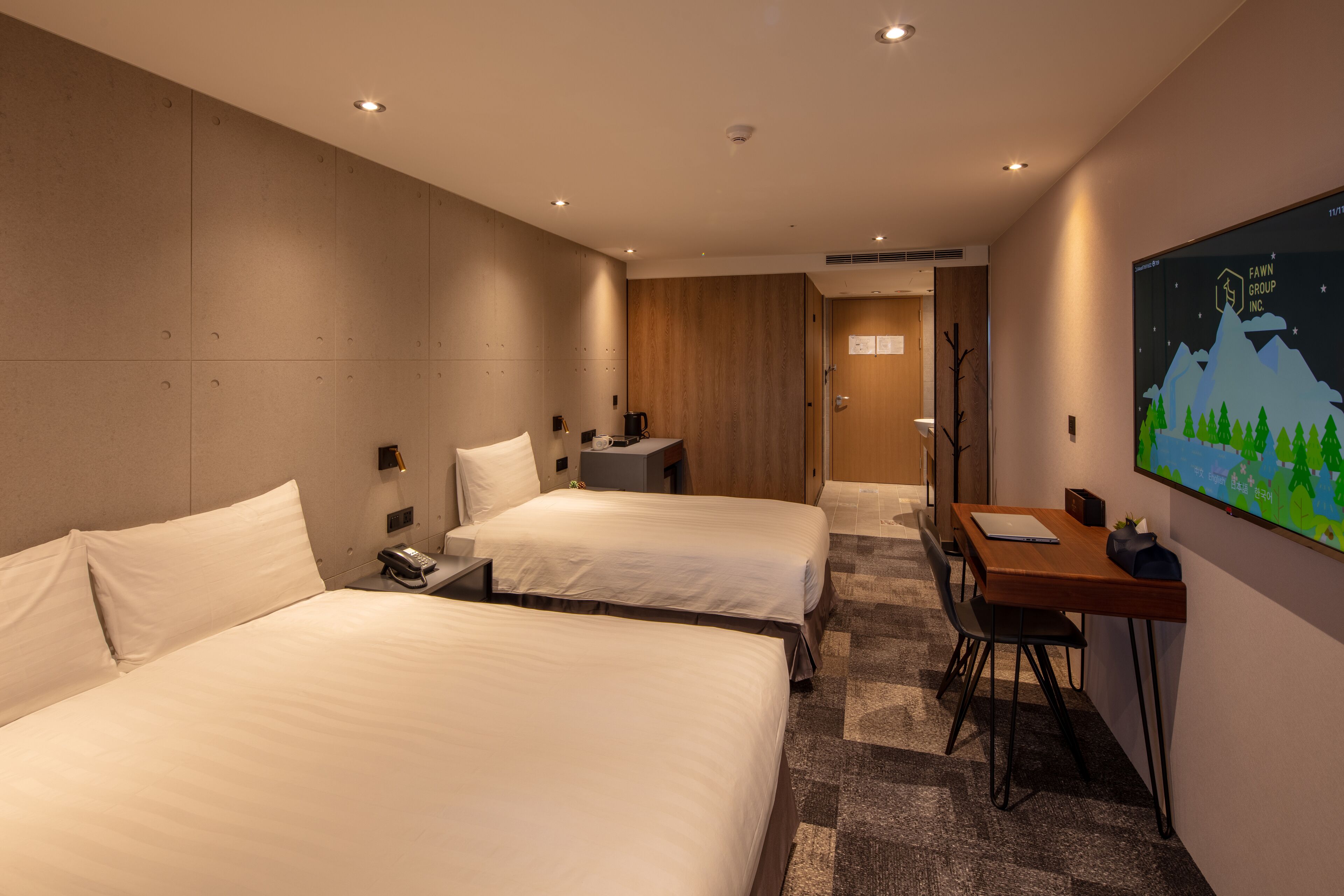 A hotel room with two beds, a desk, a chair, and a wall-mounted TV.