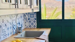 Une cuisine avec une grande fenêtre, un évier et un saladier rempli de citrons sur le plan de travail.