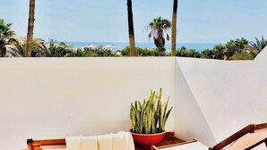Un balcon avec vue sur la mer, une plante en pot et des chaises en bois.
