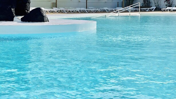 Una piscina azul cristalina con sillones de descanso blancos y una formación rocosa.