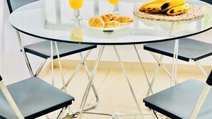 Una mesa redonda de vidrio con dos vasos de zumo de naranja, un plato de cruasanes y una cesta de plátanos.