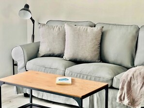 A grey sofa with two cushions, a wooden coffee table with a book, and a floor lamp.