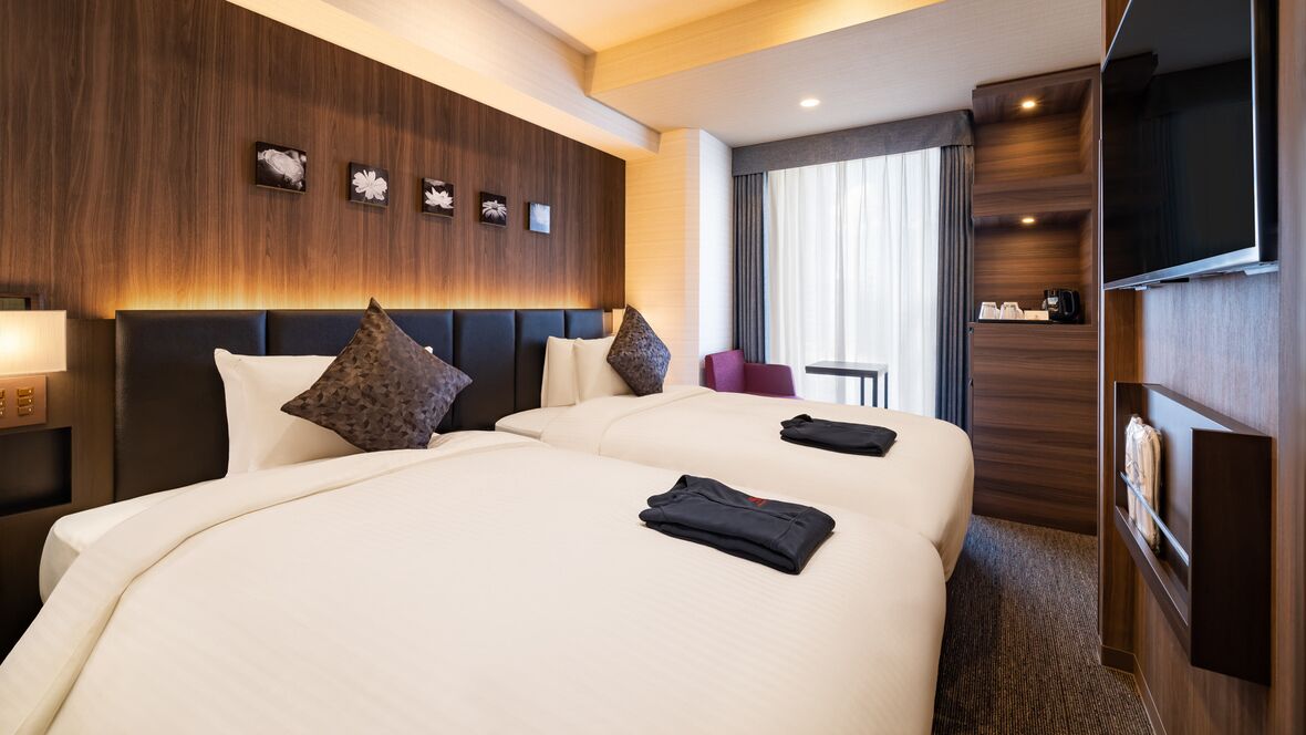 Quarto de hotel com duas camas grandes, televisão, escrivaninha e área de estar com vista para a cidade.