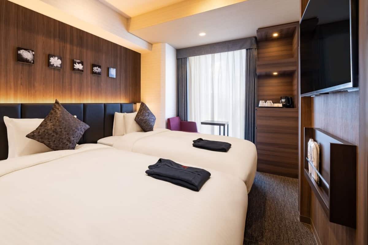 A hotel room with two large beds, a TV, a desk, and a seating area with a view of the city.