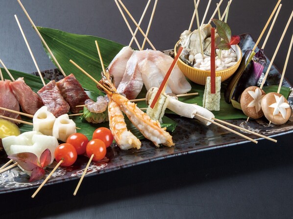 Diversos mariscos y vegetales ensartados sobre un plato negro.