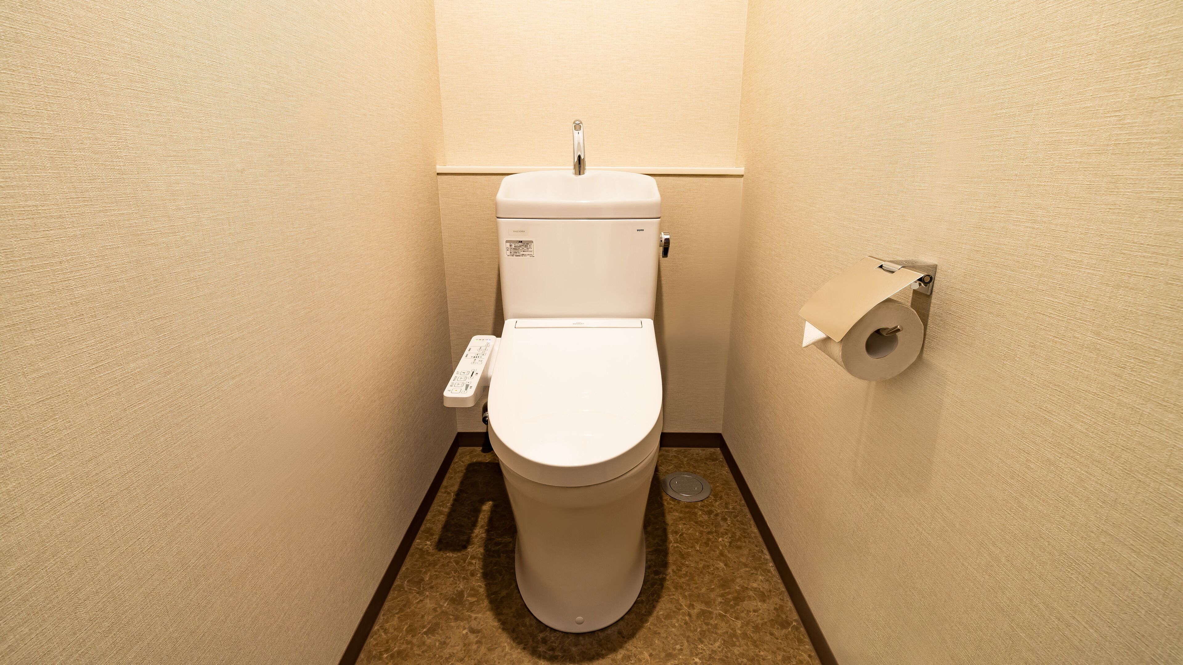 A small, clean bathroom with a toilet, a paper towel holder, and a flush handle.