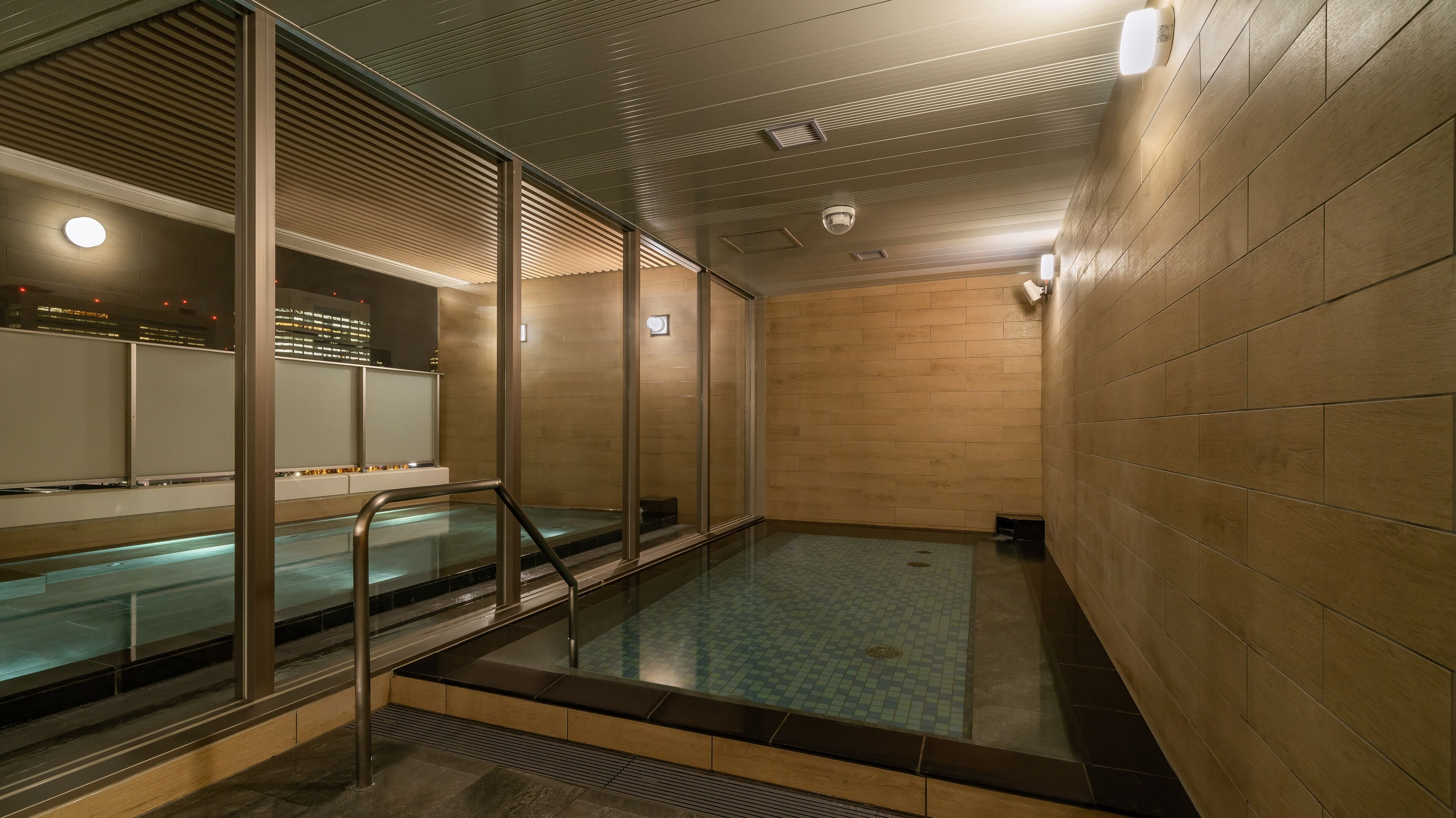 A modern indoor swimming pool with glass walls and a wooden floor.