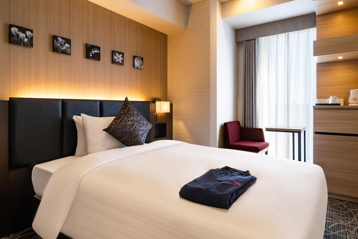 A hotel room with a large bed, a red chair, a small table, and a minibar.