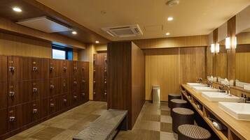 A hotel bathroom with multiple lockers, a bench, and a row of sinks with mirrors.