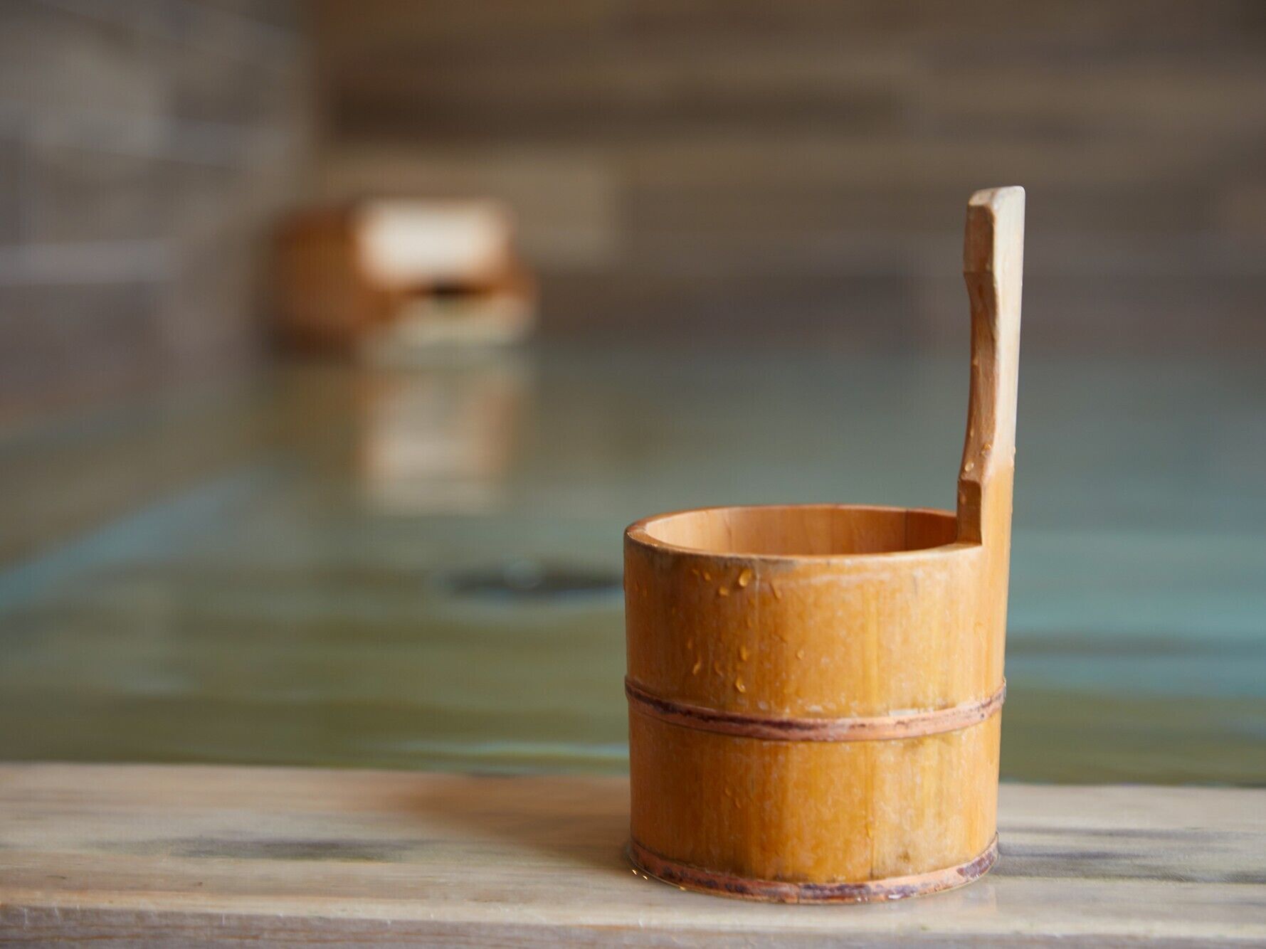 A small wooden bucket with a handle on a marble surface.