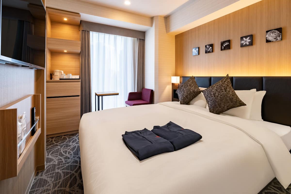 A hotel room with a large bed, a TV, a desk with a lamp, and a chair.