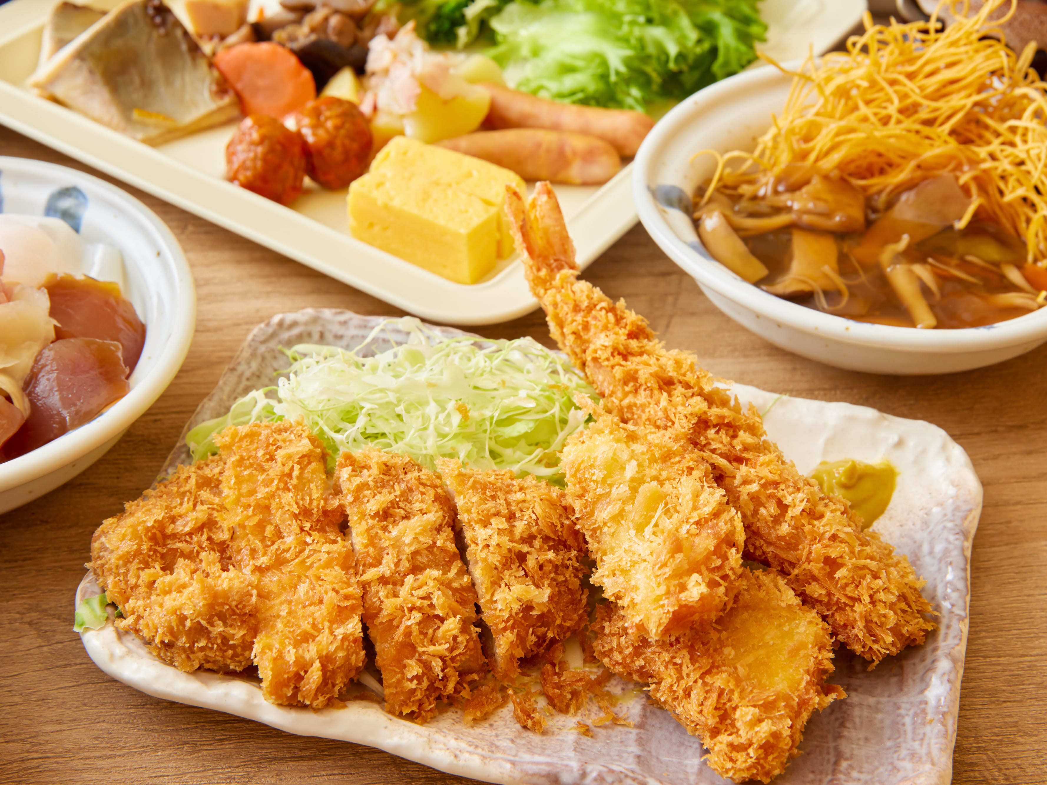 A variety of dishes including fried items, vegetables, and noodles on a wooden table.