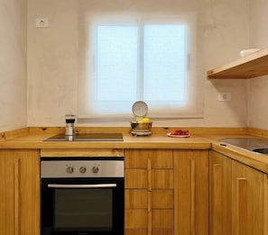 A compact kitchen with wooden cabinets, a stove, a sink, and a window with blinds.