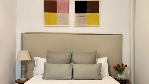 Un lit bien fait, avec une tête de lit beige, une lampe de chevet et un vase rempli de fleurs rouges.