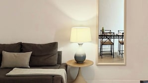 Un salon moderne avec un canapé, une table ronde surmontée d’une lampe et un grand miroir accroché au mur.