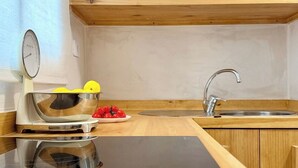 Une cuisine dotée d’un plan de travail en bois, d’un évier en acier inoxydable, d’une balance et d’un saladier contenant des citrons et des tomates.