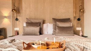 A neatly made bed with a woven basket containing breakfast items, a wooden headboard, and wall-mounted lamps. - Canaryislandshost l The Sky Suites (Tinajo)