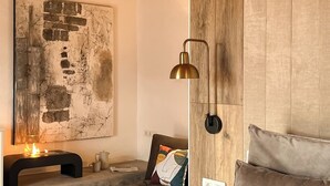 A cozy bedroom with a large bed, a bedside table with a lamp, a fireplace, and a rustic wooden headboard. - Canaryislandshost l The Sky Suites (Tinajo)