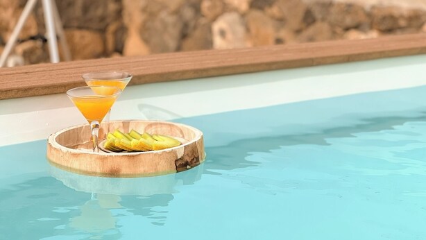 A poolside setting with a wooden tray holding a martini glass and a cocktail, and a tripod in the background. - Canaryislandshost l The Sky Suites (Tinajo)