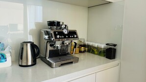 Et køkken med kaffemaskine, elkedel og forskellige beholdere på bordet.