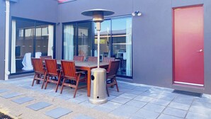 En terrasse med et bord, stole, en skraldespand og en dør.