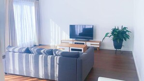 En moderne stue med en hjørnesofa, et fladskærms-tv, et lille sofabord og en potteplante.