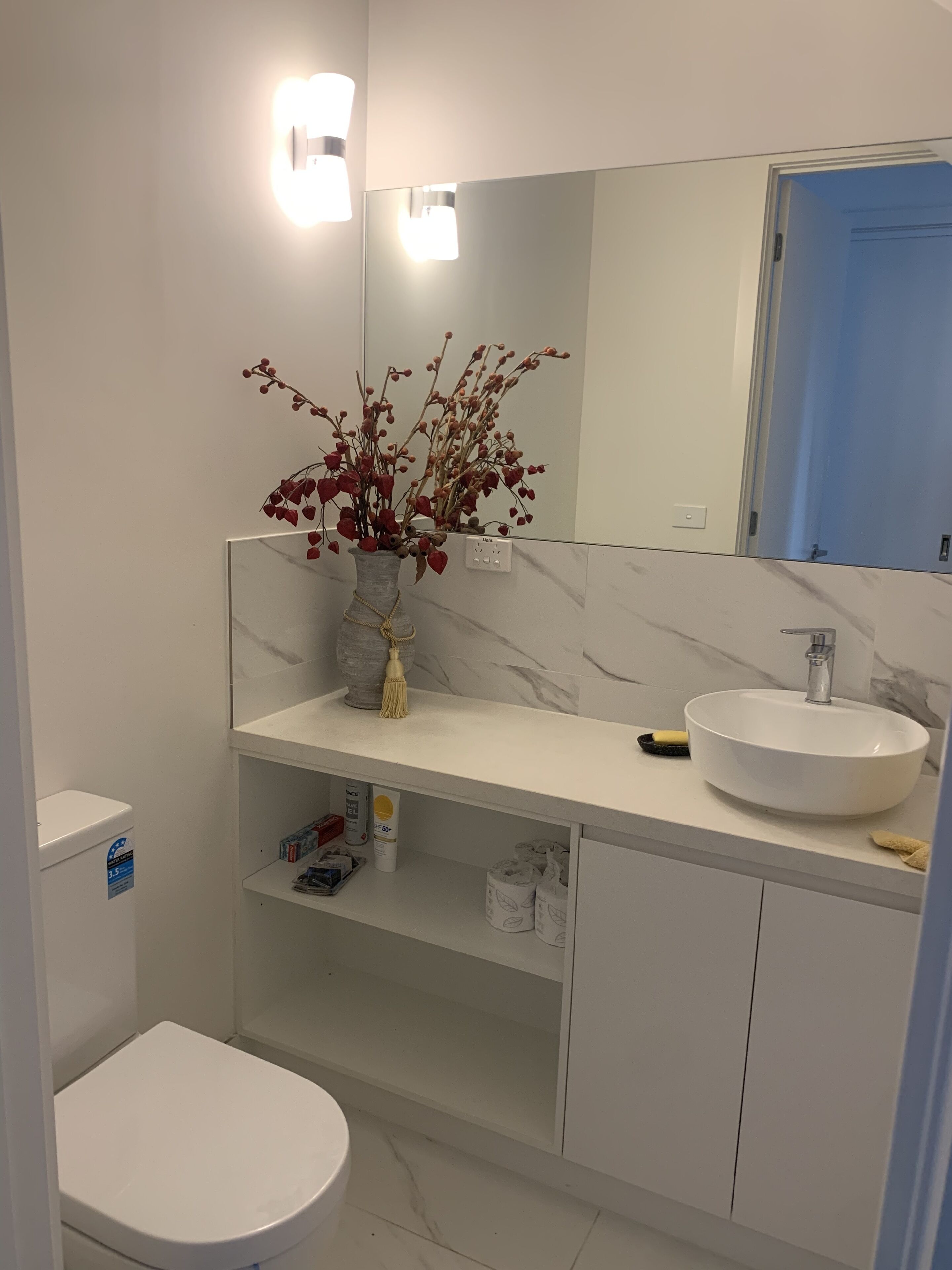 A modern bathroom with a white toilet, a marble sink, and a mirror above the sink.