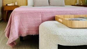 A neatly made bed with a pink blanket and pillows, a wooden headboard, and a bedside table with a lamp.