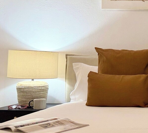 Una cama bien tendida con almohadas blancas y marrones, una lámpara en una mesita de noche y una revista sobre la cama.