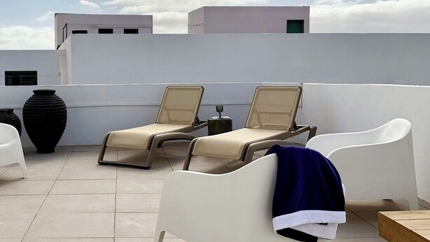 Eine Dachterrasse mit Lounge-Möbeln, einem Tisch und einer großen Vase.