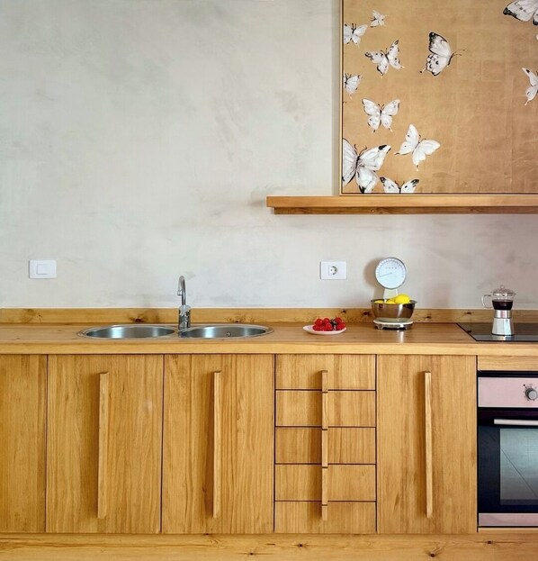 A kitchen with wooden cabinets, a stainless steel sink, a coffee maker, and a wall-mounted shelf with butterflies.