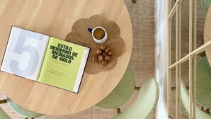 Ein runder Holztisch mit einem Buch mit dem Titel 'ESTILO MODERNO DE MEDIADOS DE SIGLO 1940-1959' und einer Kaffeetasse.