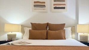 Ein ordentlich bezogenes Bett mit vier braunen Kissen, zwei an der Wand befestigten abstrakten Kunstwerken und je einer Nachttischlampe auf beiden Seiten.