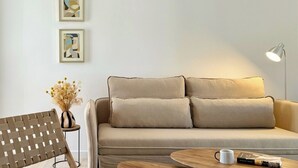 A modern living room with a beige sofa, a wooden coffee table, and a woven chair. There are two abstract paintings on the wall and a vase with dried flowers on a side table. - Canaryislandshost l Sol (Puerto del Carmen)