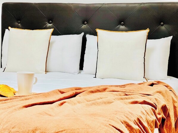 A bed with a tufted headboard, white pillows, a brown blanket, and a white cup.