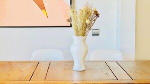 Et konferencelokale med et hvidt vase med tørrede blomster, to hvide stole og et billede i ramme på væggen.