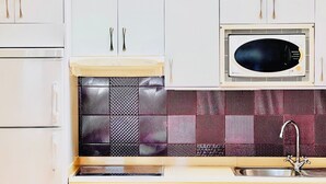 Et køkken med hvide skabe, en mikrobølgeovn, et mønstret backsplash og en vask.