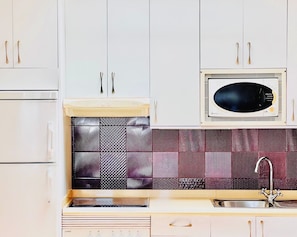 A kitchen with white cabinets, a microwave, a patterned backsplash, and a sink.