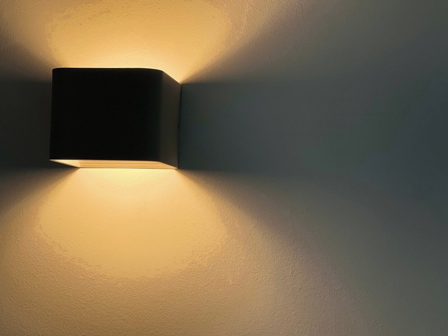 A wall-mounted light fixture casting a warm glow on a plain wall.