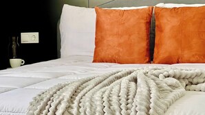 Una cama bien hecha con almohadas blancas y naranjas, una colcha blanca y un enchufe de pared.